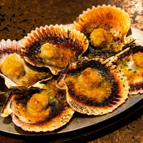 A plate of grilled scallops in their shells, topped with butter and herbs.