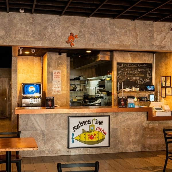 Interior of Submarine Crab restaurant with dining tables, a service counter, and visible kitchen.